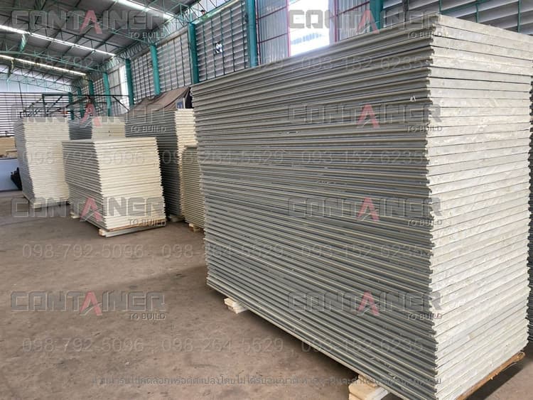 Insulated sandwich panels for the walls and roof of prefabricated units, stacked on pallets in the factory with the insulation core visible at the edge
