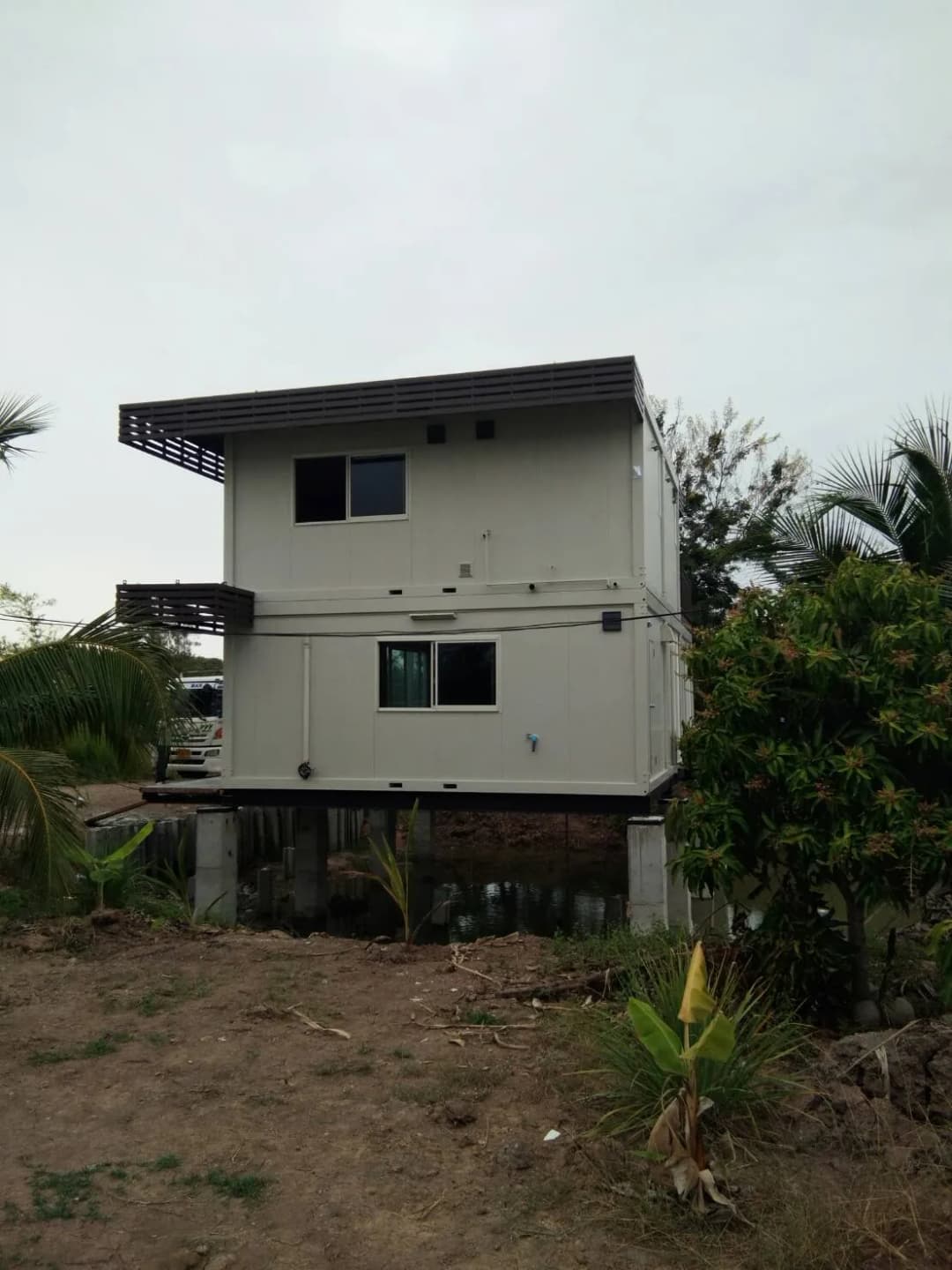 水辺の2階建てノックダウンハウス。1階はガラス張り、鉄骨階段、池の上のコンクリート柱に設置(3枚目)