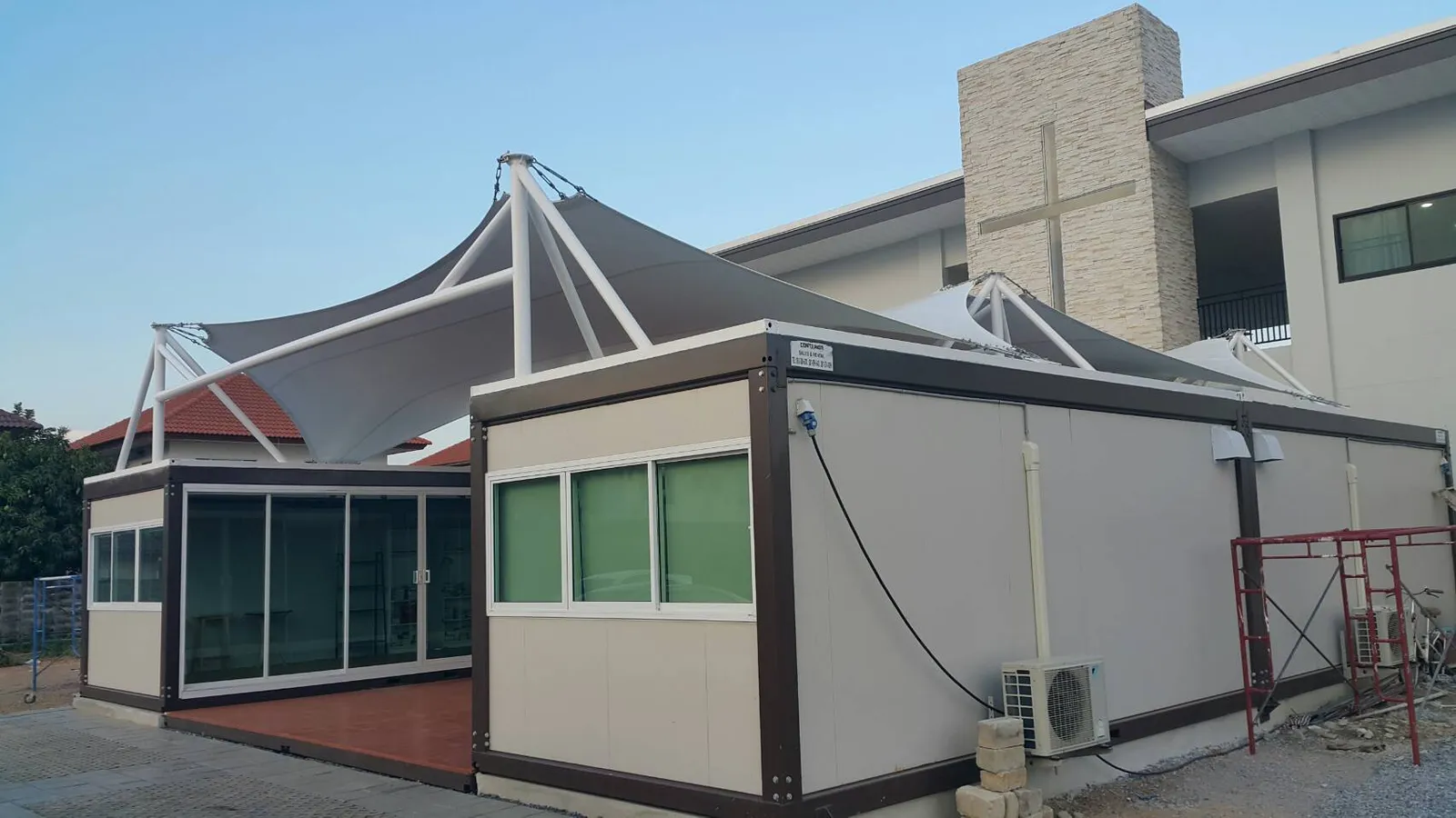 Knock-down hall: two rows of cream units with a wooden deck between and a white tensile-fabric roof, in front of a church (view 3)