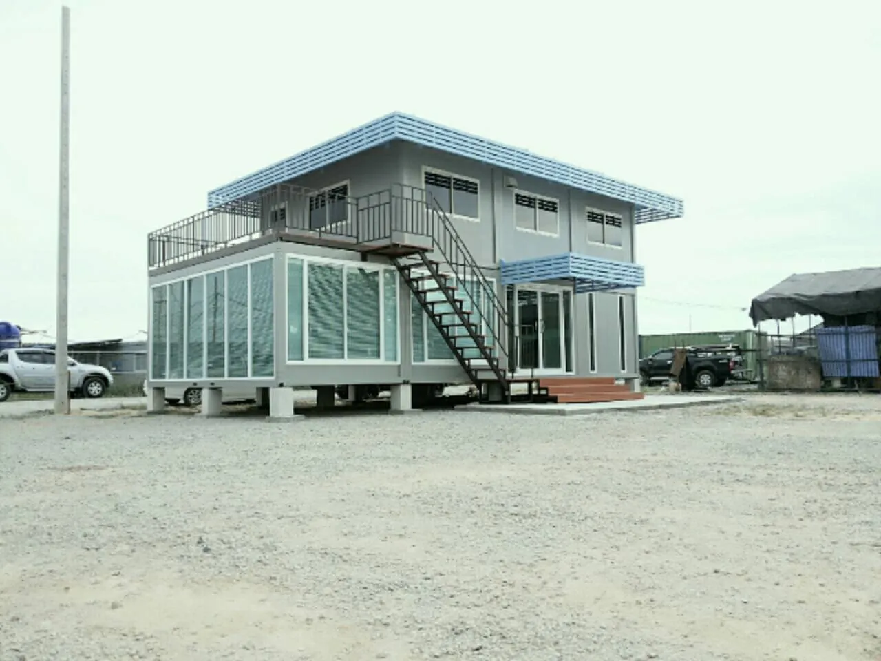 Grey two-storey knock-down house with light-blue louvres and a projecting glass room
