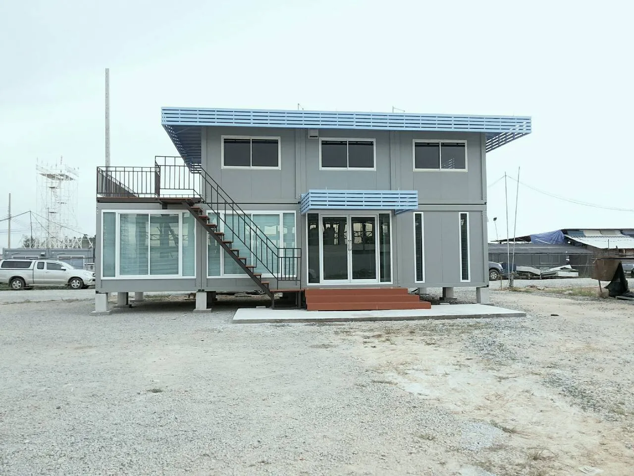Grey two-storey knock-down house with light-blue louvres and a projecting glass room (view 2)