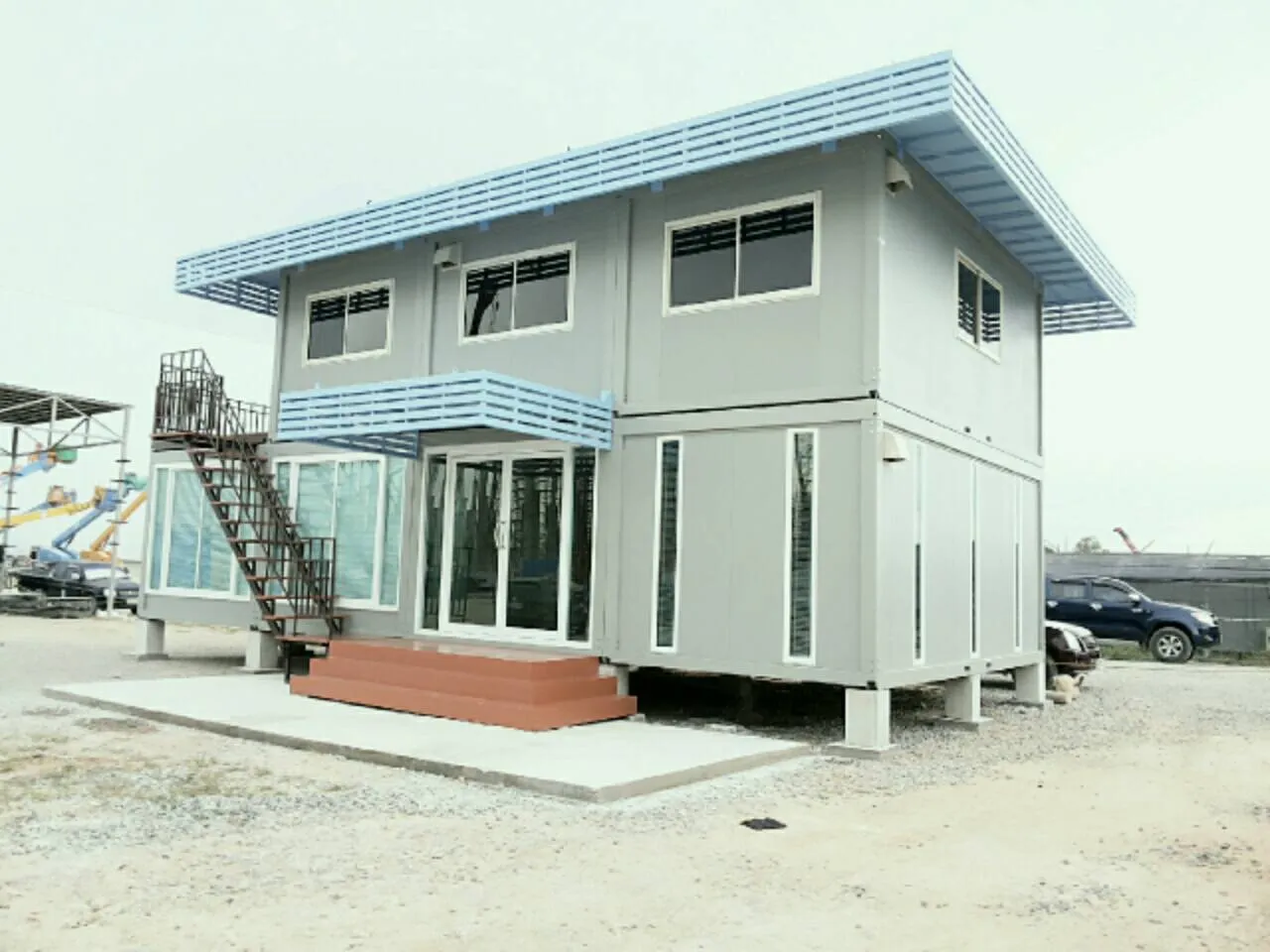 Grey two-storey knock-down house with light-blue louvres and a projecting glass room (view 3)