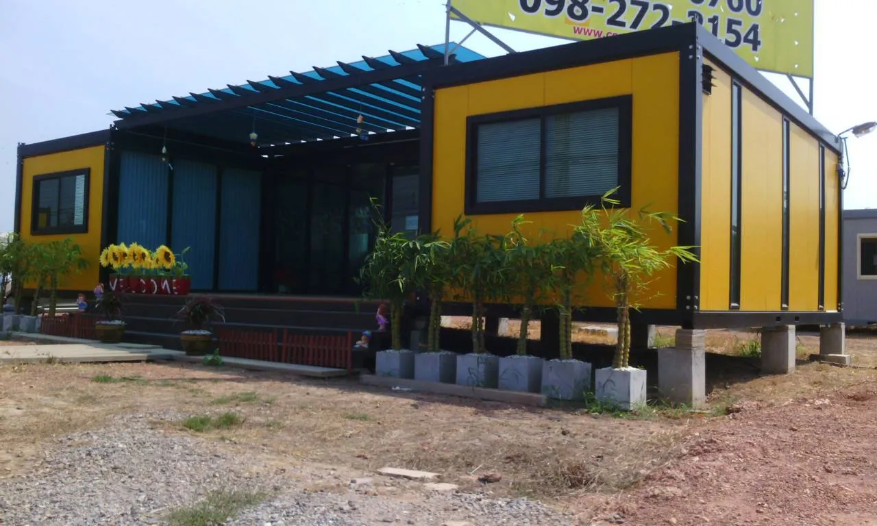 Knock-down sales office: two yellow units flanking a glass hall with a blue steel pergola