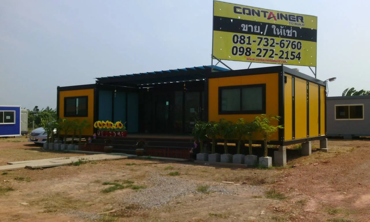 Knock-down sales office: two yellow units flanking a glass hall with a blue steel pergola (view 2)