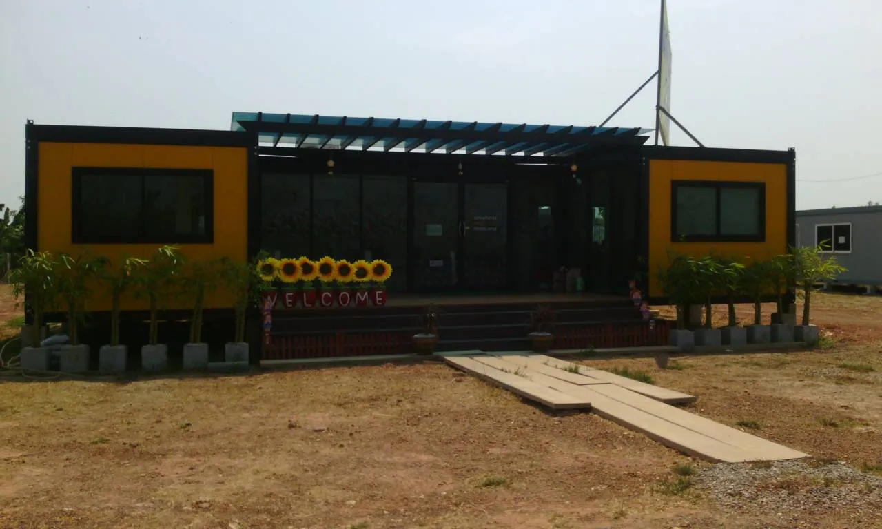 Knock-down sales office: two yellow units flanking a glass hall with a blue steel pergola (view 3)