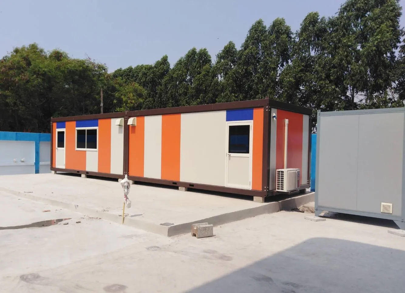 Knock-down worker housing joined in a long row with orange, white and blue striped walls on a concrete yard