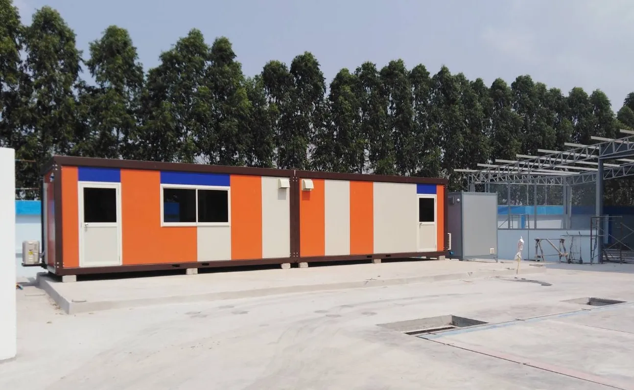 Knock-down worker housing joined in a long row with orange, white and blue striped walls on a concrete yard (view 3)