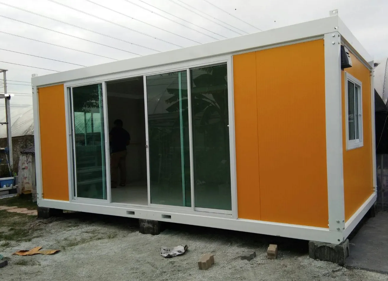 Knock-down office unit with orange walls and white frame, a person standing beside it for scale (view 2)