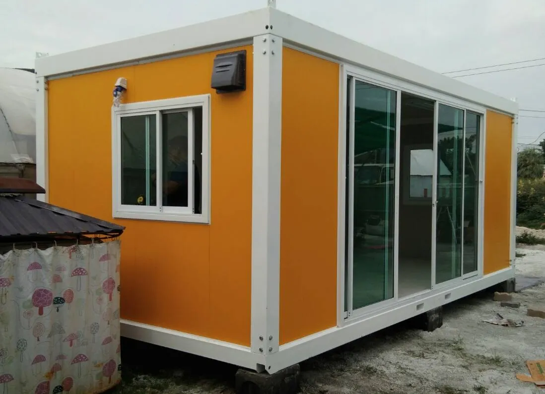 Knock-down office unit with orange walls and white frame, a person standing beside it for scale (view 3)