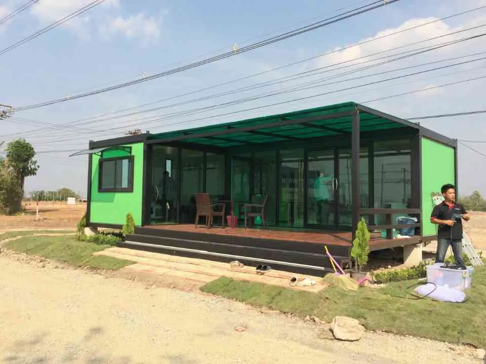 Knock-down café with bright green walls, full glass front, polycarbonate roof and a wooden deck with tables