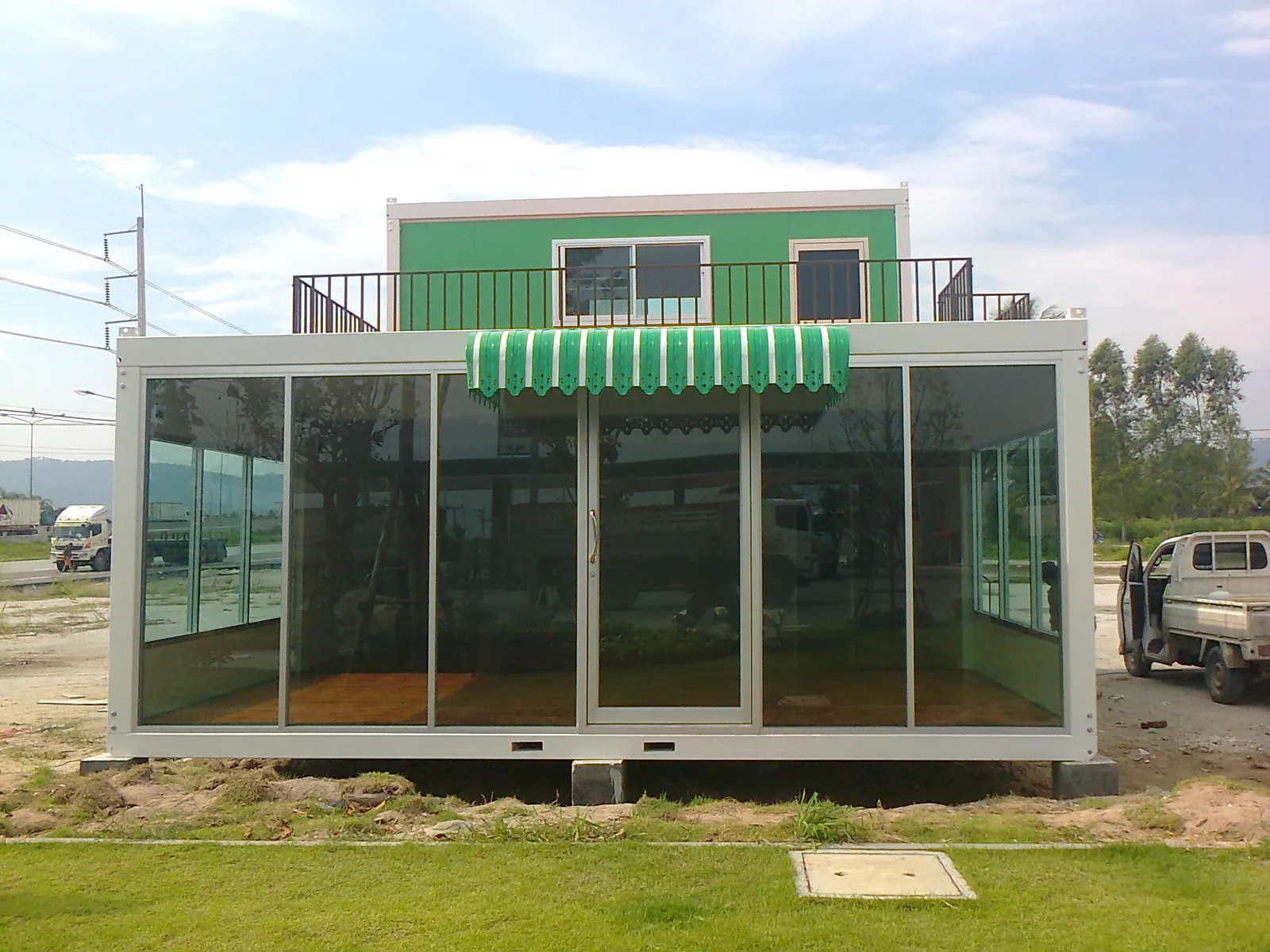 Green two-storey knock-down building with a single-storey glass café attached and a striped awning (second view)
