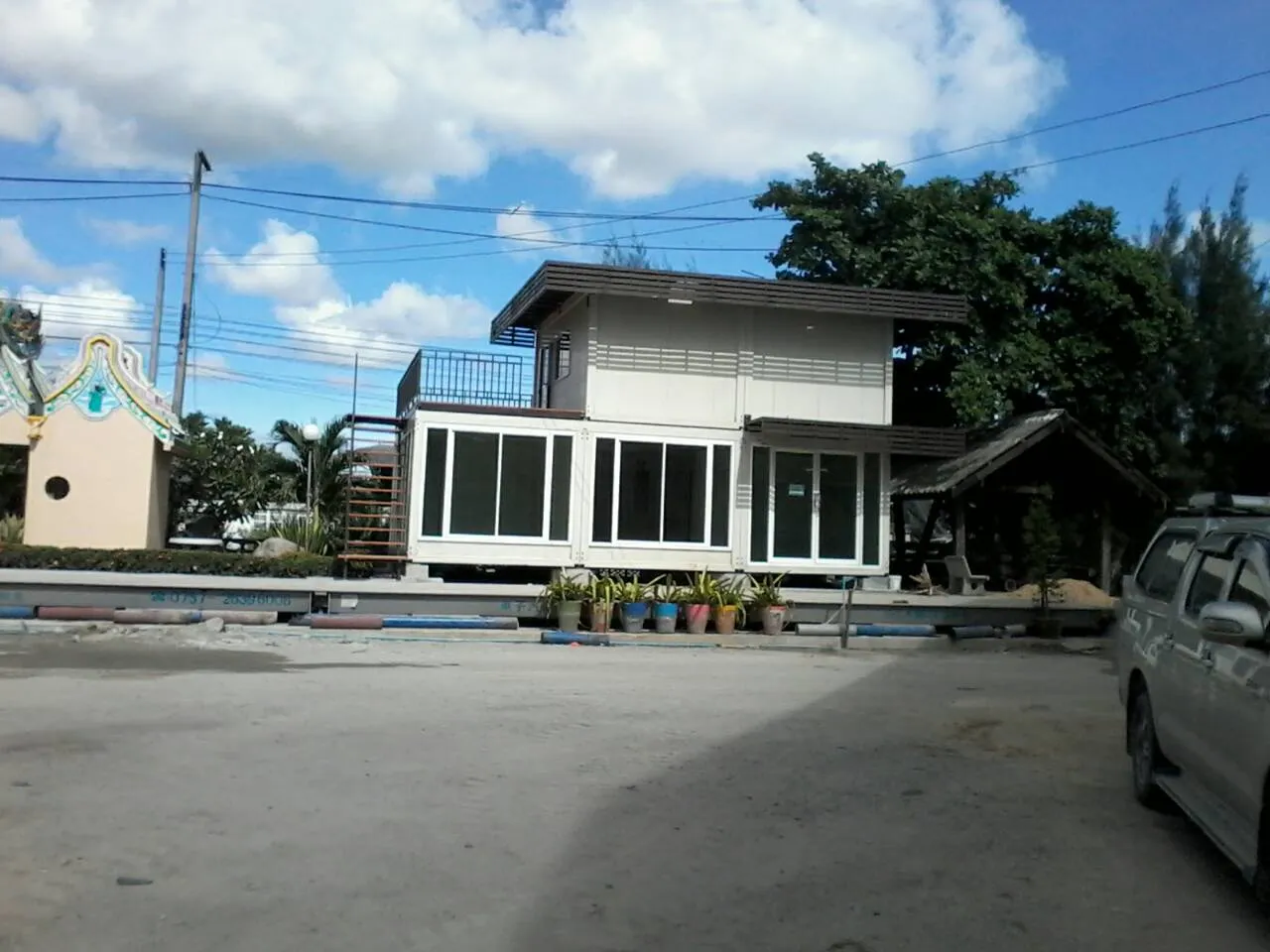 Two-storey knock-down house in white and dark brown with sun louvres and an upper balcony, set in a garden (second view)