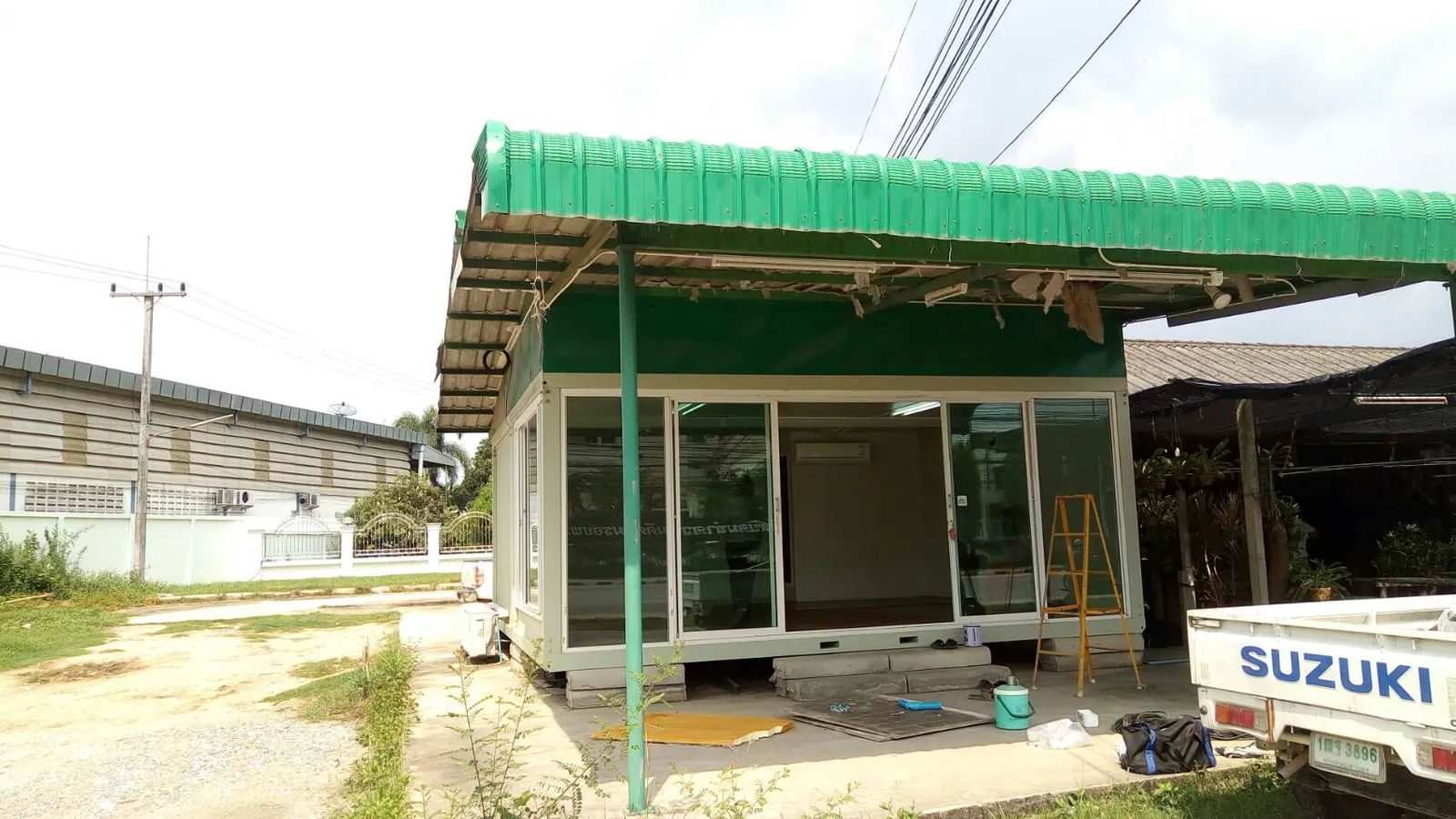 Knock-down shop with sliding glass under a curved green metal-sheet roof, during installation