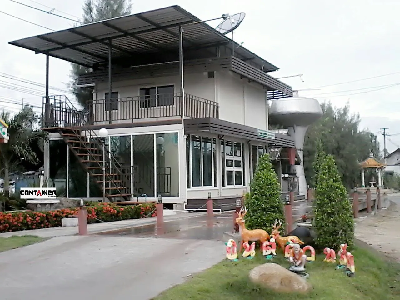 Two-storey knock-down house with balcony under a separate steel canopy roof